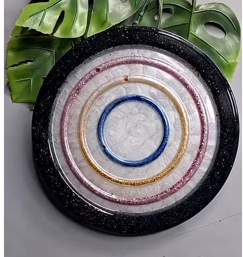 Decorative plate with concentric colored rings (blue center, gold and pink rings) and a black rim, placed on a surface with green leaves in the background. - Bling On Decor® | Luxury Handmade Home Decor ANJU BALA