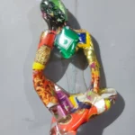 Sculpture made from colorful candy wrappers forming a humanoid figure with a green head on a gray surface. - Bling On Decor® | Luxury Handmade Home Decor ANJU BALA