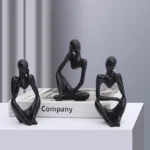 Three black abstract figurines in thoughtful poses on a white surface beside a book labeled 'Company'. - Bling On Decor® | Luxury Handmade Home Decor ANJU BALA