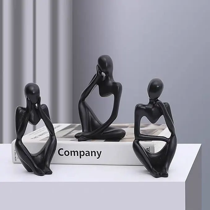 Three black abstract figurines in thoughtful poses on a white surface beside a book labeled 'Company'. - Bling On Decor® | Luxury Handmade Home Decor ANJU BALA
