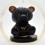 Glossy black bear figurine with a gold 'W' emblem on its chest, on a wooden pedestal, framed by a pale laurel border. - Bling On Decor® | Luxury Handmade Home Decor ANJU BALA