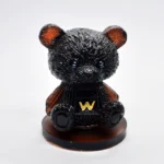 Close-up of a glossy black bear figurine with red inner ears and a yellow W on its chest, standing on a brown base. - Bling On Decor® | Luxury Handmade Home Decor ANJU BALA