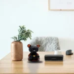 Potted plant in a tall ceramic vase on a light wood desk, with a glossy black teddy bear figurine and a Bose speaker nearby. - Bling On Decor® | Luxury Handmade Home Decor ANJU BALA