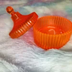Orange ribbed plastic jar with a matching lid resting beside it on a soft pastel surface. - Bling On Decor® | Luxury Handmade Home Decor ANJU BALA