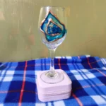 Unleash-the-Sparkle-Blue-Geode-Wine-Glass-8.webp - Bling On Decor® | Luxury Handmade Home Decor Wine glass holding a blue and copper art piece on a white padded stand atop a blue plaid blanket. - Bling On Decor® | Luxury Handmade Home Decor ANJU BALA