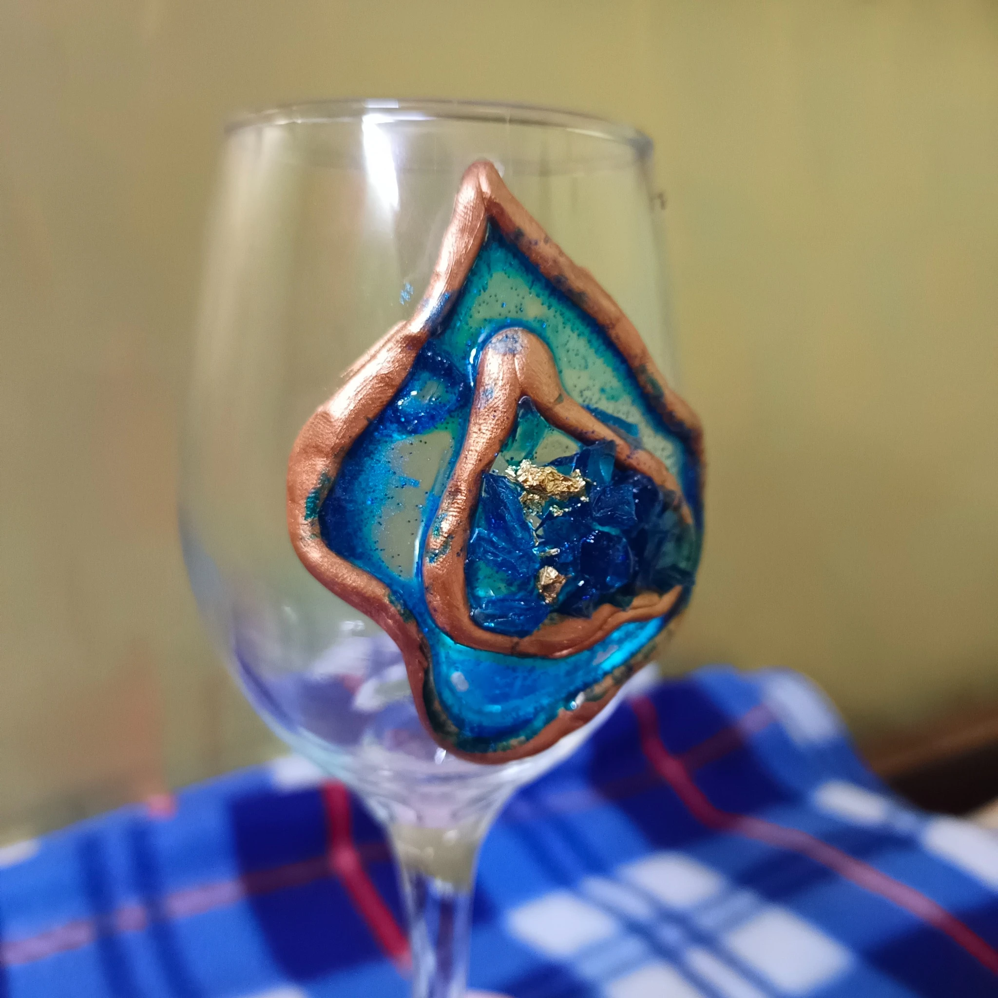 Unleash-the-Sparkle-Blue-Geode-Wine-Glass-9.webp - Bling On Decor® | Luxury Handmade Home Decor Close-up of a colorful hand-painted glass ornament with blue, teal, and copper accents inside a clear glass container. - Bling On Decor® | Luxury Handmade Home Decor ANJU BALA