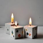 Three square terrazzo candles with colorful geometric flecks, lit and burning on a light gray surface. - Bling On Decor® | Luxury Handmade Home Decor ANJU BALA