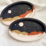 Two oval decorative trays with a night-sky design: dark background, white moon, and layered gold, beige, orange, and white waves. - Bling On Decor® | Luxury Handmade Home Decor ANJU BALA