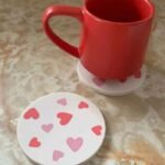 Red ceramic mug resting on a white heart-decorated coaster on a marble table, with a matching lid nearby. - Bling On Decor® | Luxury Handmade Home Decor ANJU BALA