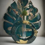 Artistic still life: teal circular ring with gold flecks surrounding a glass bottle holding dried grasses, set against a teal leaf backdrop. - Bling On Decor® | Luxury Handmade Home Decor ANJU BALA