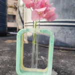 Pink bougainvillea blooms in a tall glass vase placed inside a mint-green chair outdoors, with an industrial backdrop. - Bling On Decor® | Luxury Handmade Home Decor ANJU BALA