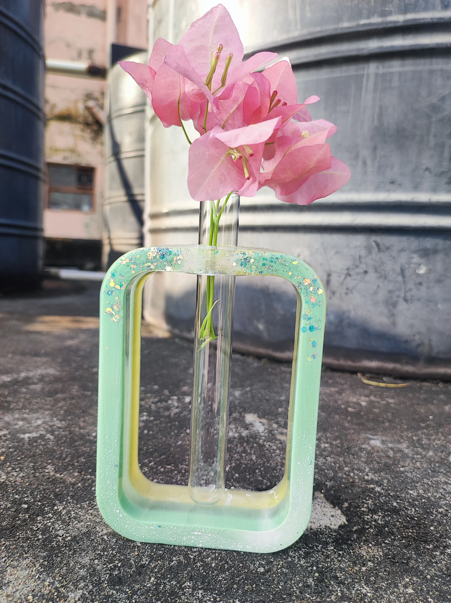 Pink bougainvillea blooms in a tall glass vase placed inside a mint-green chair outdoors, with an industrial backdrop. - Bling On Decor® | Luxury Handmade Home Decor ANJU BALA