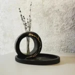 🖤-Handmade-Luxury-Black-Resin-Kintsugi-Ring-Vase-with-Tray.webp - Bling On Decor® | Luxury Handmade Home Decor Black circular sculpture with a hollow ring and a vase of dried stems, resting on a round base against a textured wall. - Bling On Decor® | Luxury Handmade Home Decor ANJU BALA
