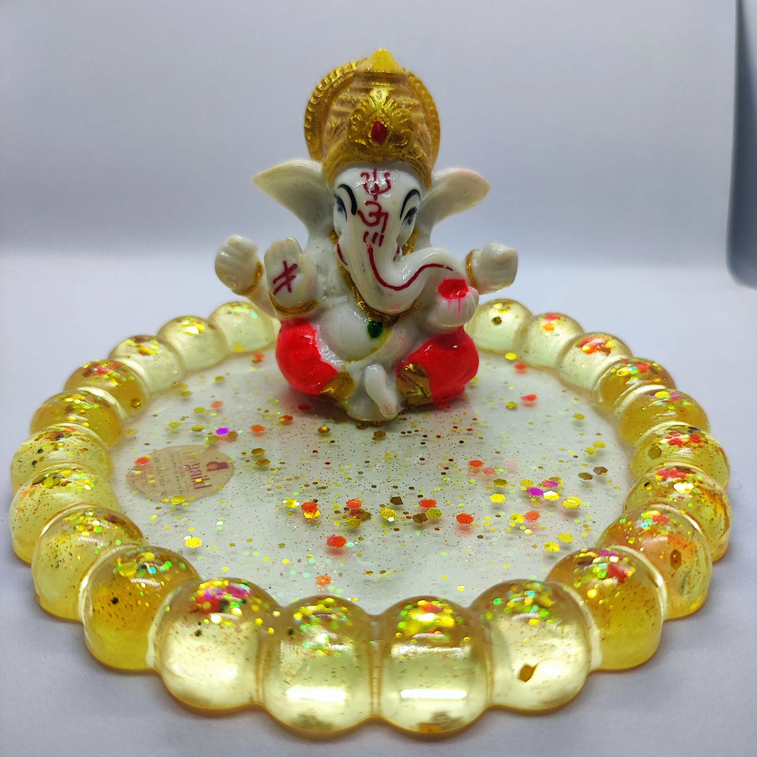 Bling-on®-handmade-lord-ganesha-resin-diya-holder-luxury-pooja-decor-decorative-oil-lamp-s-4-scaled-1webp - Bling On Decor® | Luxury Handmade Home Decor Small painted figure of Lord Ganesha with a gold crown, seated on a plate covered in yellow beads and festive confetti, red markings on the trunk. - Bling On Decor® | Luxury Handmade Home Decor ANJU BALA