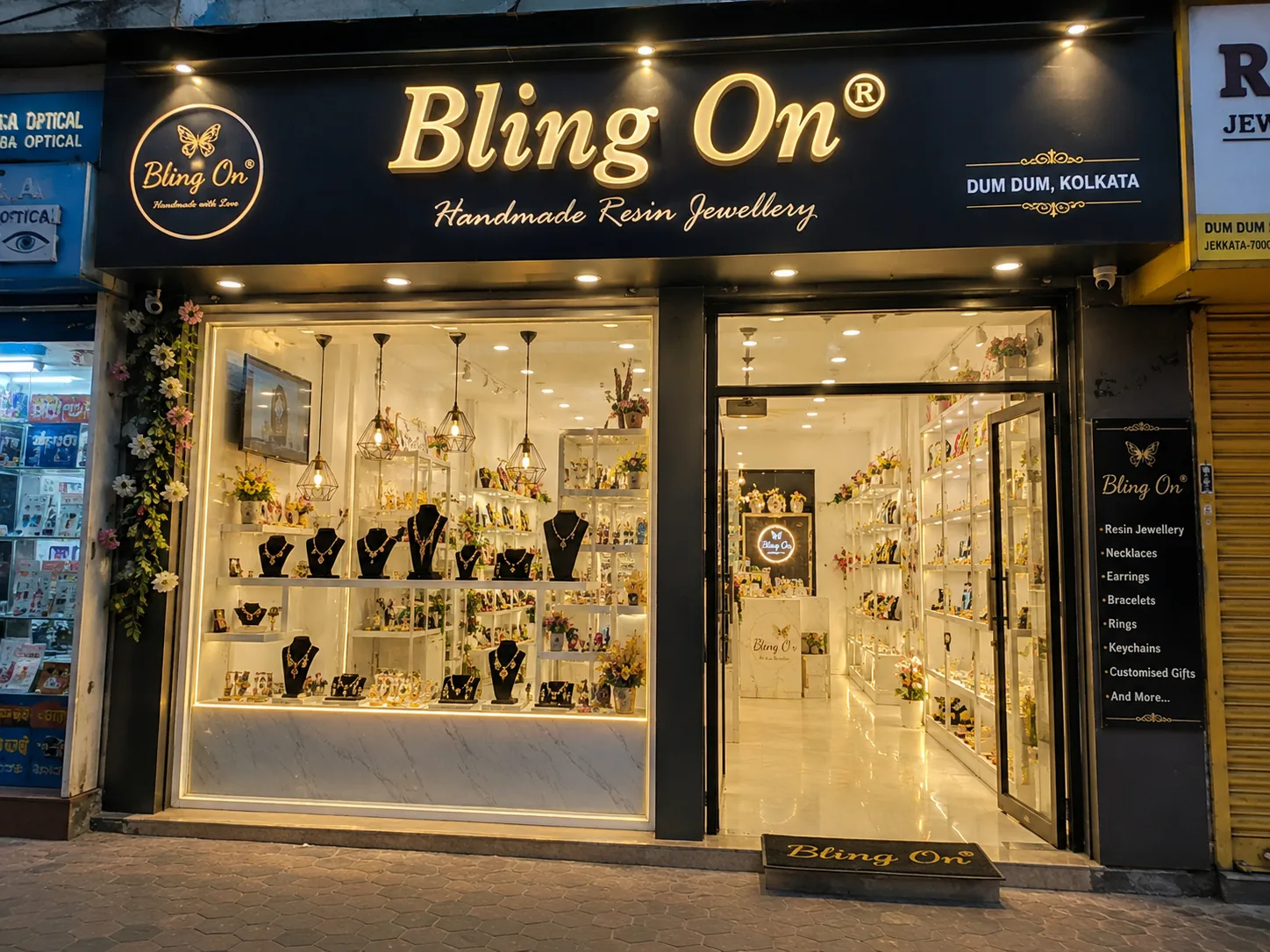 Front of Bling On, a handmade resin jewellery shop, with glass display windows full of necklaces and earrings in view. Exterior of Bling On store at night with glowing sign and showroom filled with jewelry displays. Shop window displays jewelry on black busts and shelves, entrance to Bling On. Boutique storefront for Bling On Resin Jewellery, with bright interior lighting and products arranged on shelves. Doorway into Bling On jewellery store, gold-toned sign, mannequins with necklaces behind glass. - Bling On Decor® | Luxury Handmade Home Decor ANJU BALA - Bling On Decor® | Luxury Handmade Home Decor ANJU BALA